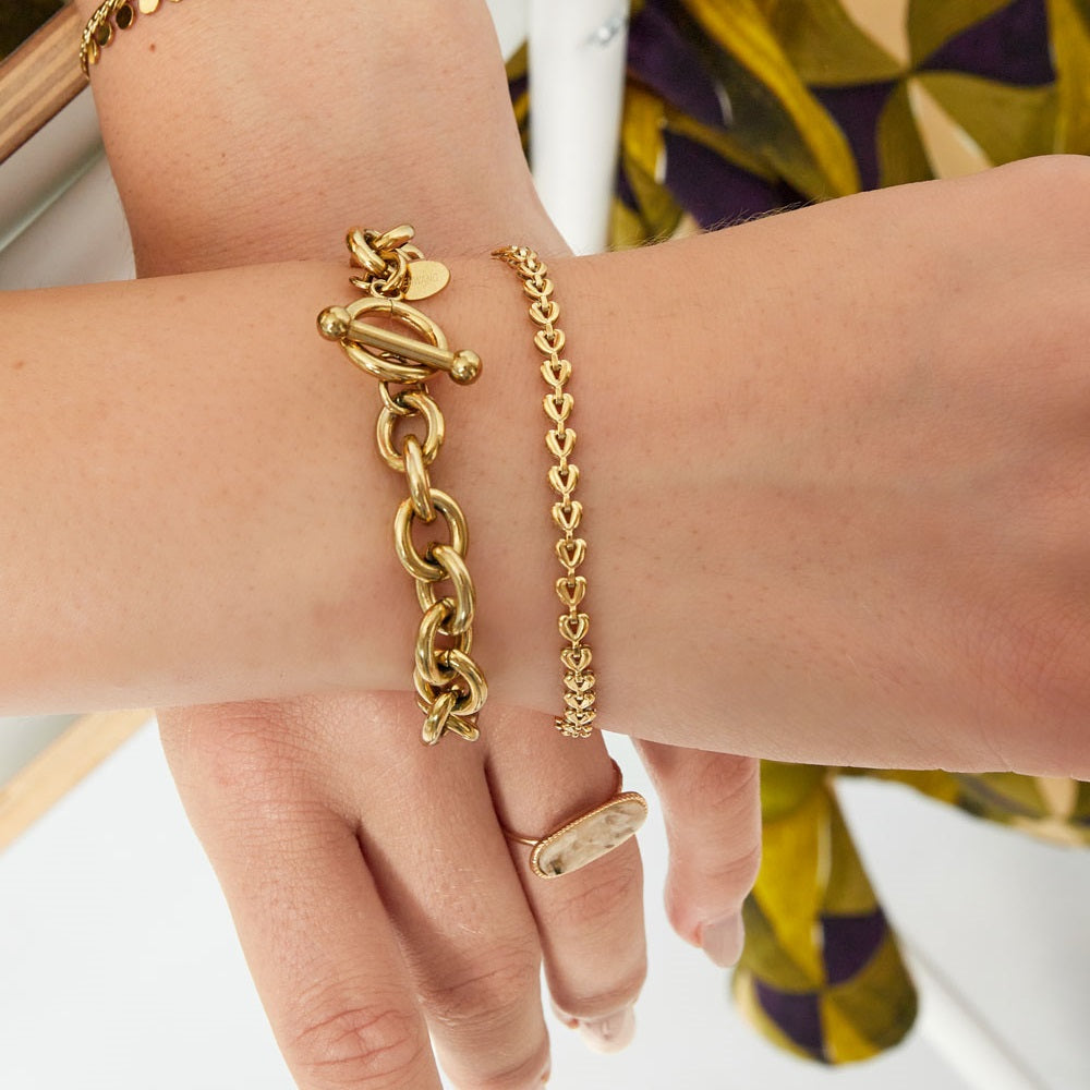 Arm met armbandjes, het rechter armbandje is het armbandje Linked Hearts Goud. Dit armbandje is gemaakt van stainless steel, hierdoor is hij nikkelvrij en waterrpoof. Shop dit armbandje nu op www.jenelry.com