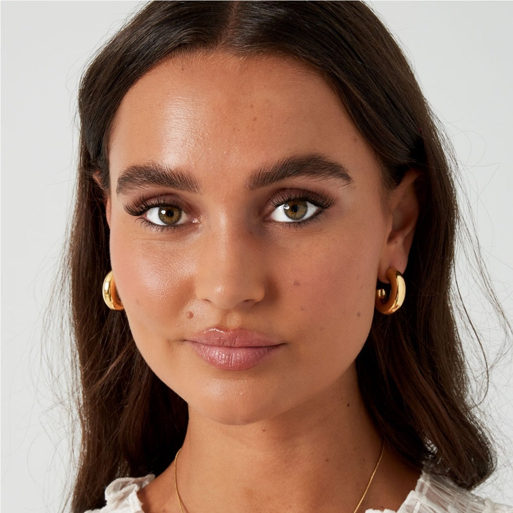 Vrouw met grove musthave oorbellen in het goud. Deze grove, chunky hoops zijn waterproof en verkleuren niet als ze in aanraking komen met water. Shop deze oorbellen nu op www.jenelry.com